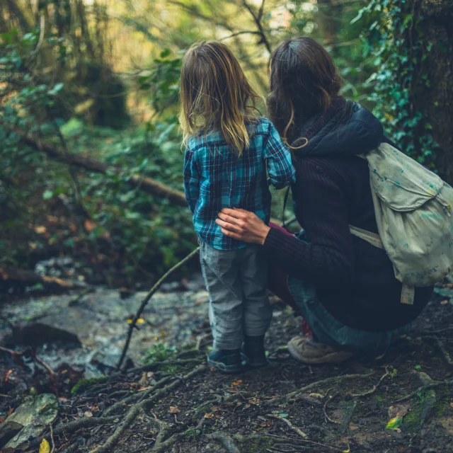 A young mother and her toddler are resting by a brook in the woods